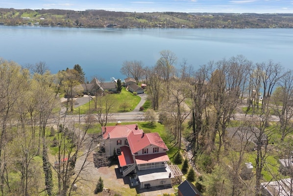 Stunning aerial view of a red-roofed home nestled in lush greenery, offering direct access to the serene lakefront—perfect for tranquil living or vacation getaways.