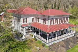Experience tranquility in this classic Finger Lakes home, complete with a striking red roof and serene wraparound porch nestled in lush surroundings. Ideal for a peaceful getaway.