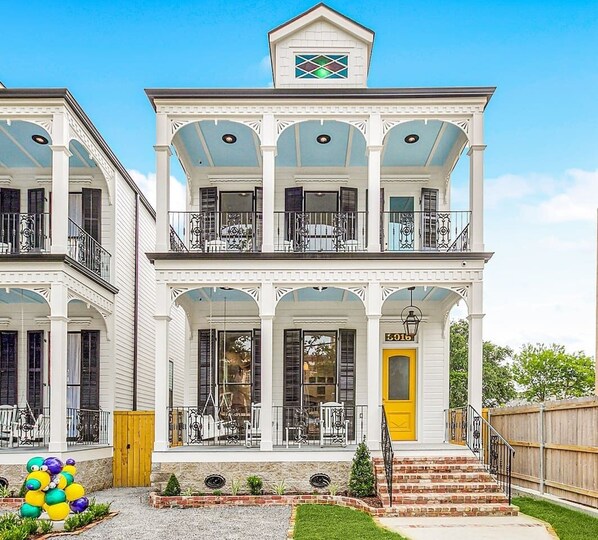 The front view of one of our two 5-bedroom, 5-bath homes on world-famous Canal Street, featuring the iconic "MARDI GRAS BEAD DOG" statue, offers a captivating scene with streetcars passing by.