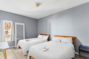 A modern, spacious bedroom with two full beds, a crib, and a 32" Roku TV. 
