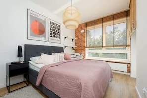 A bright, minimalist bedroom with a large bed covered in a pink duvet, surrounded by sunlight streaming in through large windows, and decorated with simple yet elegant decor.