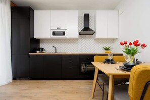 A sleek, modern kitchen with black and white cabinetry, a wood-finished dining table set with tableware and a bouquet of red tulips, giving a warm and inviting look.