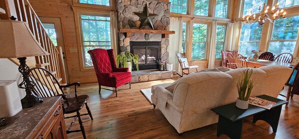 Gather around the stone fireplace in this inviting living room with large windows offering stunning views of the surrounding nature.
