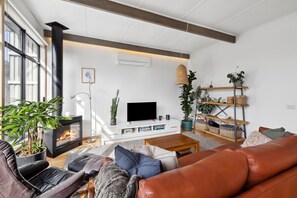 A bright, north-facing living area with plush seating, a Smart TV, and air conditioningg