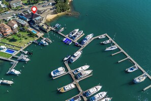 Aerial view of a marina with various boats docked, adjacent to waterfront properties. The property is marked with a red pin, indicating its prime location near the water