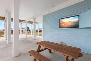 Fun, outdoor area with streaming TV, two picnic tables, bar area with seating, mini frig, and sink
