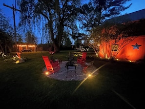Firepit at night surrounded by accent lighting with one of two pergolas in view