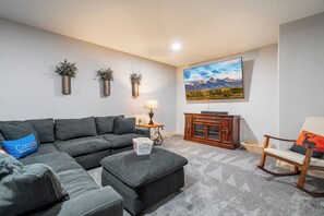 Settle into the plush sectional and enjoy a movie night in this inviting basement retreat, complete with a large TV, warm lighting, and plenty of space to relax.