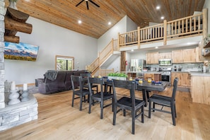 This beautifully designed space features a modern rustic kitchen, large dining table, and cozy living area under soaring wood ceilings with a charming loft above.