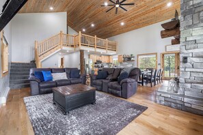 The open-concept living space boasts vaulted wood ceilings, a cozy stone fireplace, and plush seating, making it the perfect gathering spot for friends and family.