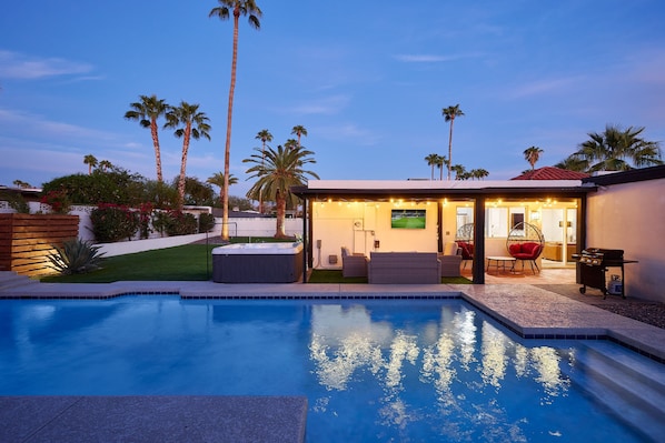 Private backyard featuring a pool, hot tub, BBQ grill, lounge chairs, mini golf, and a patio with a Smart TV, fire pit and outdoor dining area that seats 6 guests.