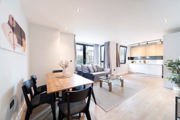 Open-plan living area and kitchen with a sofa bed, TV, dining table, and six chairs.
