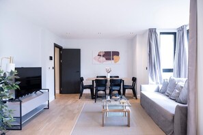 Open-plan living area and kitchen with a sofa bed, TV, dining table, and six chairs.