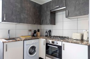 Fully equipped kitchen with washing machine, stovetop, oven, fridge, kettle, and toaster.