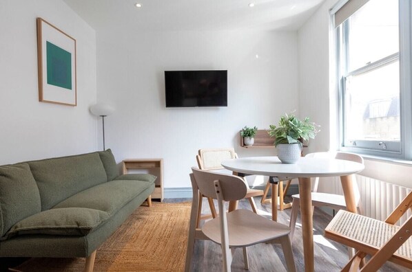 Open-plan living area with kitchen, sofa, TV, and workspace.