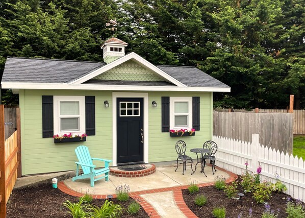 Exterior view showing brick path+patio, cottage style garden, and picket fence. 