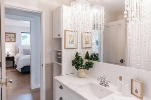 Refresh in this bright bathroom, where the large mirror and white vanity create a clean, serene space. The beaded curtain adds charm, while built-in shelves and decor invite a peaceful, personal retreat