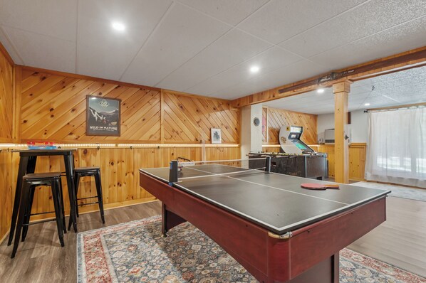 Game room has ping pong/pool table, foosball table, Arcade game, couches, TV