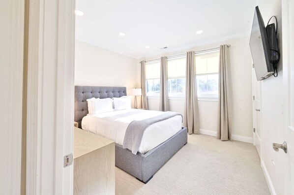 Bright and spacious bedroom featuring a comfortable plush bed, flat-screen TV, and large windows for plenty of natural light.
