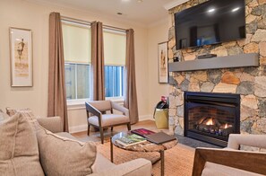 Cozy living room with a stone fireplace, comfortable seating, and a flat-screen TV for a warm and inviting atmosphere.