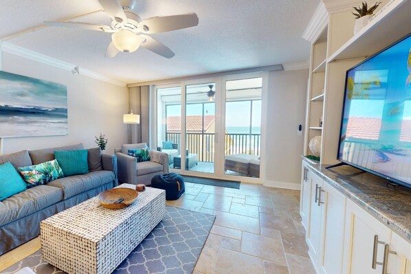The spacious living room is designed for relaxation, featuring a comfortable sofa, a large flat-screen TV, & direct access to the beachfront balcony