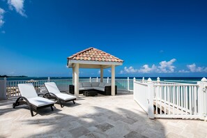 Large over-the-water deck with sun beds, a tiled cabana for shade, and a stairwell for water access. 