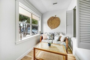 Relax in this cozy, sunlit reading nook with comfortable wicker seating and vibrant decor. Perfect for a peaceful retreat during your beach stay, this inviting corner is ideal for unwinding with a good book after a day of coastal adventures.