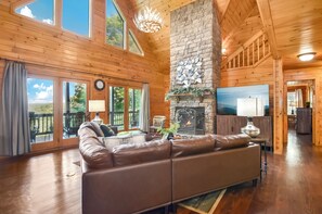 A living room area with a tall, vaulted ceiling and a large stone fireplace.