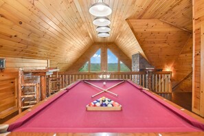Game room with a sloped wooden ceiling, featuring a centered pool table.