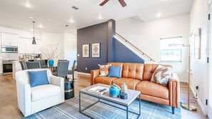 The living area offers comfort, with leather couches and chairs surrounding a smart 65" TV.