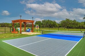 Pickleball court with fan, shaded seating, outdoor speakers, and night lighting