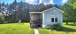 Front of cottage with deck and sitting area. Surrounded by trees.