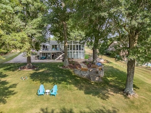 Bird's-eye view of our lakeside haven: an open backyard with lush grass, cozy fire pit area, benches, and shady trees.