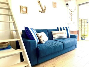 Ce salon lumineux à la décoration marine invite à la détente, avec sa lumière naturelle et son canapé confortable. Imaginez-vous ici, en train de vous relaxer après une journée à la plage. Canapé convertible en lit queen size 2 places.
