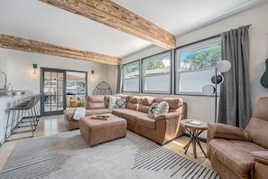 Relax in the comfortable living area off the kitchen, featuring a large L-shaped sectional, rustic wood beams, and a unique swinging chair.