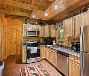 This rustic kitchen in a cabin near Pigeon Forge features stainless steel appliances, wooden cabinets, and essentials like a stove, microwave, dishwasher, and coffee maker. Ideal for a romantic, pet-friendly stay with a hot tub near Pigeon Forge.