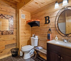 This rustic bathroom in TN features rich wood walls, a sleek vanity with soft lighting, and charming décor. Enjoy a cozy cabin-style retreat with essential amenities, perfect for a romantic, pet-friendly getaway near Pigeon Forge with a hot tub.
