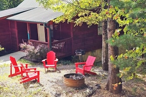 Step into serenity at this charming cabin, where the pop of red chairs adds a touch of warmth to the peaceful ambiance around the flickering fire pit. #TranquilEscape #CabinComfort #NatureTherapy 🌿🔥