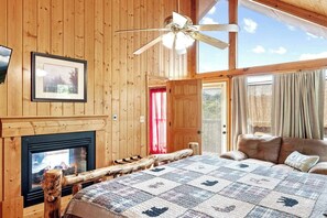 "Drift off to dreamland in this cozy cabin bedroom, where the warmth of the fireplace and the comfort of the queen size bed combine with breathtaking views through the massive glass window, all while relaxing on the plush couch."