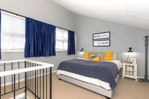 Cozy loft bedroom features a plush bed with stylish bedding, accented by bright pillows. The space is bright and inviting, offering a peaceful retreat with plenty of natural light.