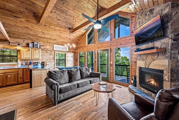 The beautiful living room includes vaulted ceilings, a gas fireplace, and large windows overlooking mountain views.