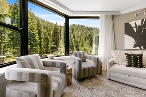 Living Room: L-shaped couch, 3 club chairs, 46” LG TV, gas fireplace, soaring windows framing impressive forested views