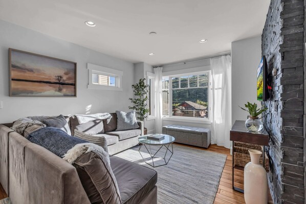 Living Room 1: L-shaped couch, Samsung TV, open layout to kitchen and dining room, main floor