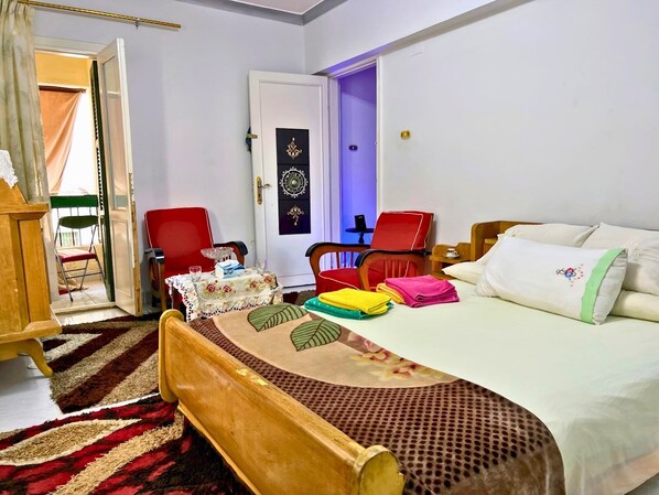 Gadou's Superior King Room features a luxurious 150x200cm orthopedic bed with premium Egyptian cotton linens, stylish cedar wood headboard, and modern workspace. Bright, airy design with blackout curtains and USB charging stations. Shared balcony access 
