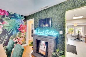 A vibrant, funky dining room with unique wallpaper, a lively grass wall, and a fun lighted sign