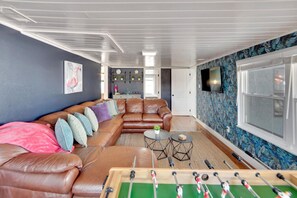 Fun and inviting living room featuring a foosball table, a large sectional sofa, a TV, and funky wallpaper that adds a playful touch to the space