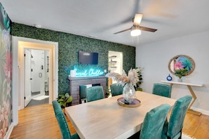 A vibrant, funky dining room with unique wallpaper, a lively grass wall, and a fun lighted sign