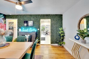 A vibrant, funky dining room with unique wallpaper, a lively grass wall, and a fun lighted sign