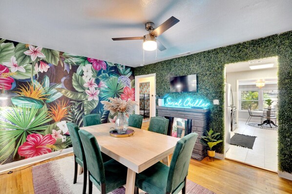 A vibrant, funky dining room with unique wallpaper, a lively grass wall, and a fun lighted sign