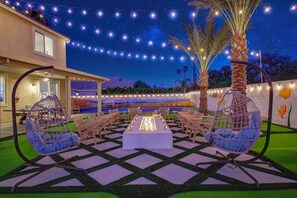 Magical outdoor setup with a long fire pit, hanging chairs, and string lights under the stars.